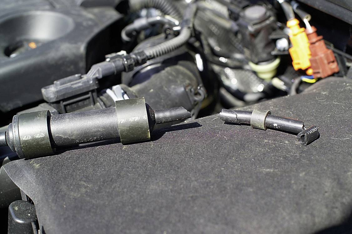 'Defekte Zündspulen auf einer Motorabdeckung platziert, mit sichtbaren Teilen des Motors im Hintergrund.'