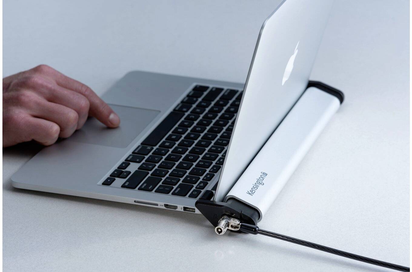 Eine Hand berührt das Trackpad eines teilweise geöffneten Laptops. Ein Sicherheitsschloss ist an der linken Ecke des Laptops befestigt.