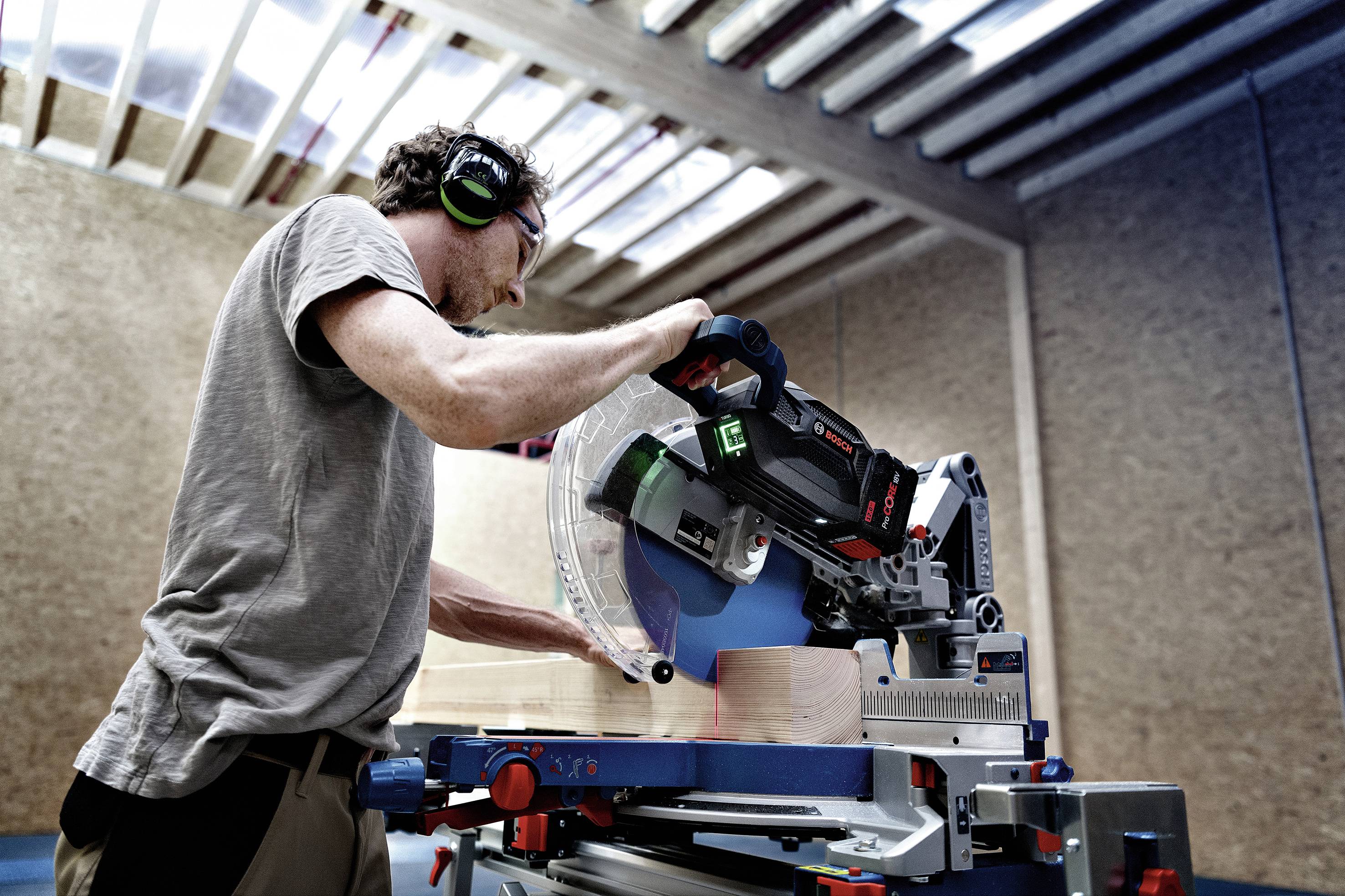 Ein Mann bedient unter Schutzvorkehrungen eine elektrische Kappsäge in einer Werkstatt, um präzise Holzstücke zuzuschneiden.