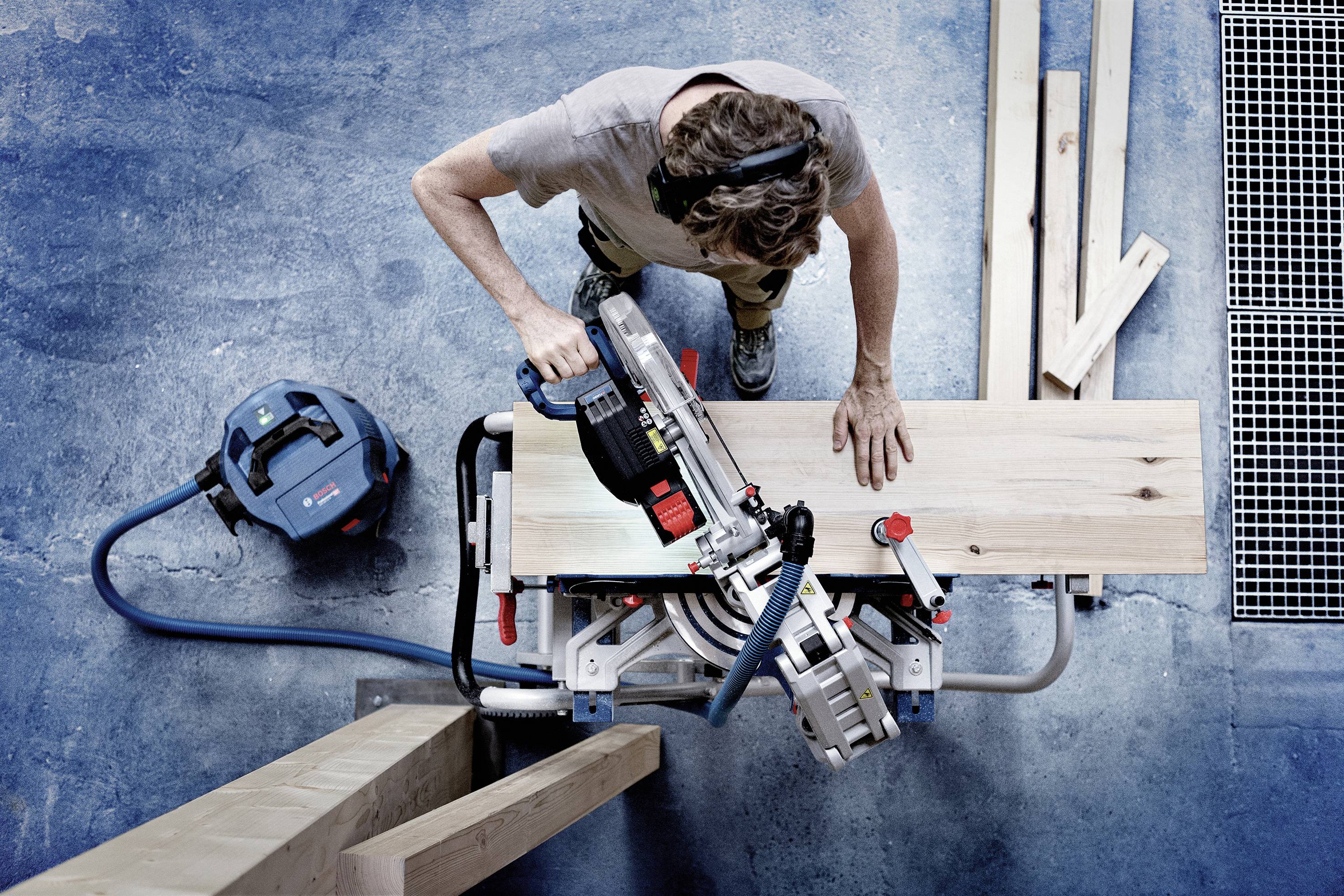 Eine Person sägt präzise ein Holzbrett mit einer elektrischen Gehrungssäge in einer Werkstattumgebung.