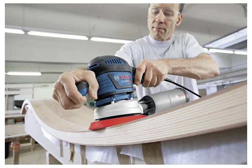 Eine Person, die in einer Werkstatt eine Exzenterschleifer verwendet, um eine geschwungene Holzoberfläche zu glätten und dabei sorgfältiges Handwerk und Detailgenauigkeit demonstriert.