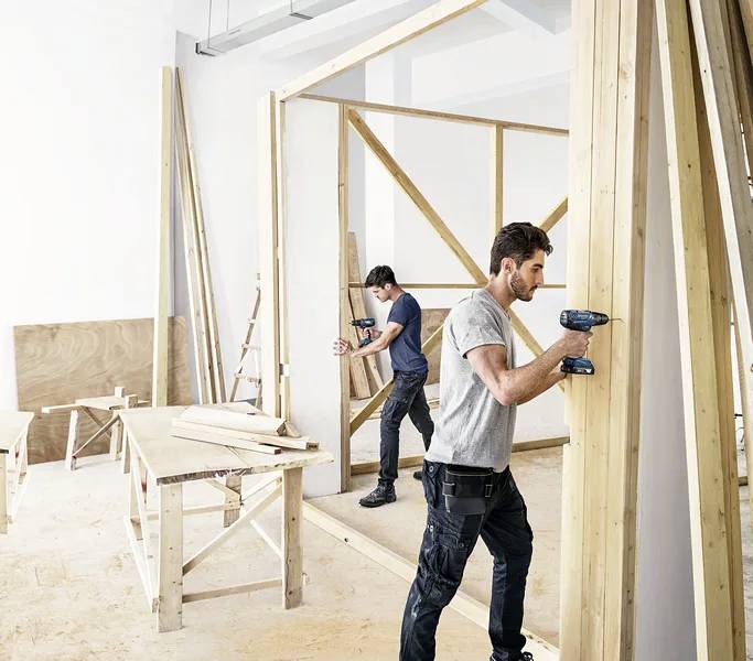 Zwei Männer, die Bohrmaschinen verwenden, um eine Holzkonstruktion in einer Werkstatt zusammenzubauen.