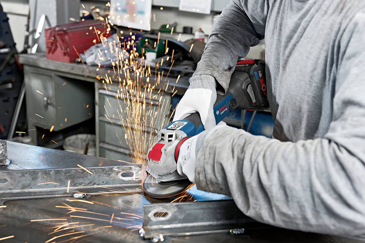 Eine Person schleift Metall an einem Arbeitstisch mit einem Winkelschleifer, Funken sprühen. Hände mit Sicherheitshandschuhen geschützt.