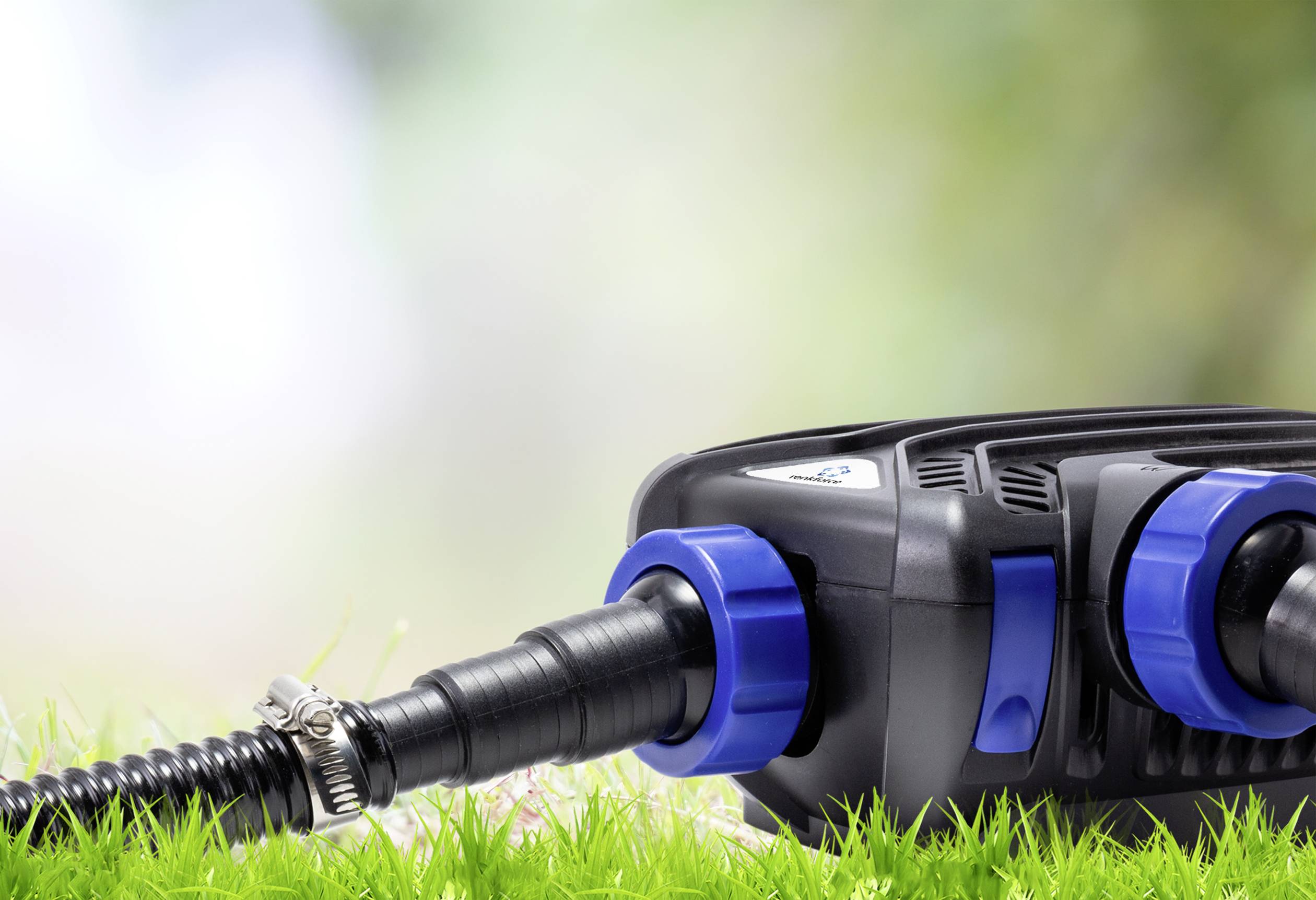 Eine schwarze Pumpe mit blauen Anschlüssen liegt auf grünem Gras, verbunden mit einem Schlauch, bereit für die Wasserpflege.