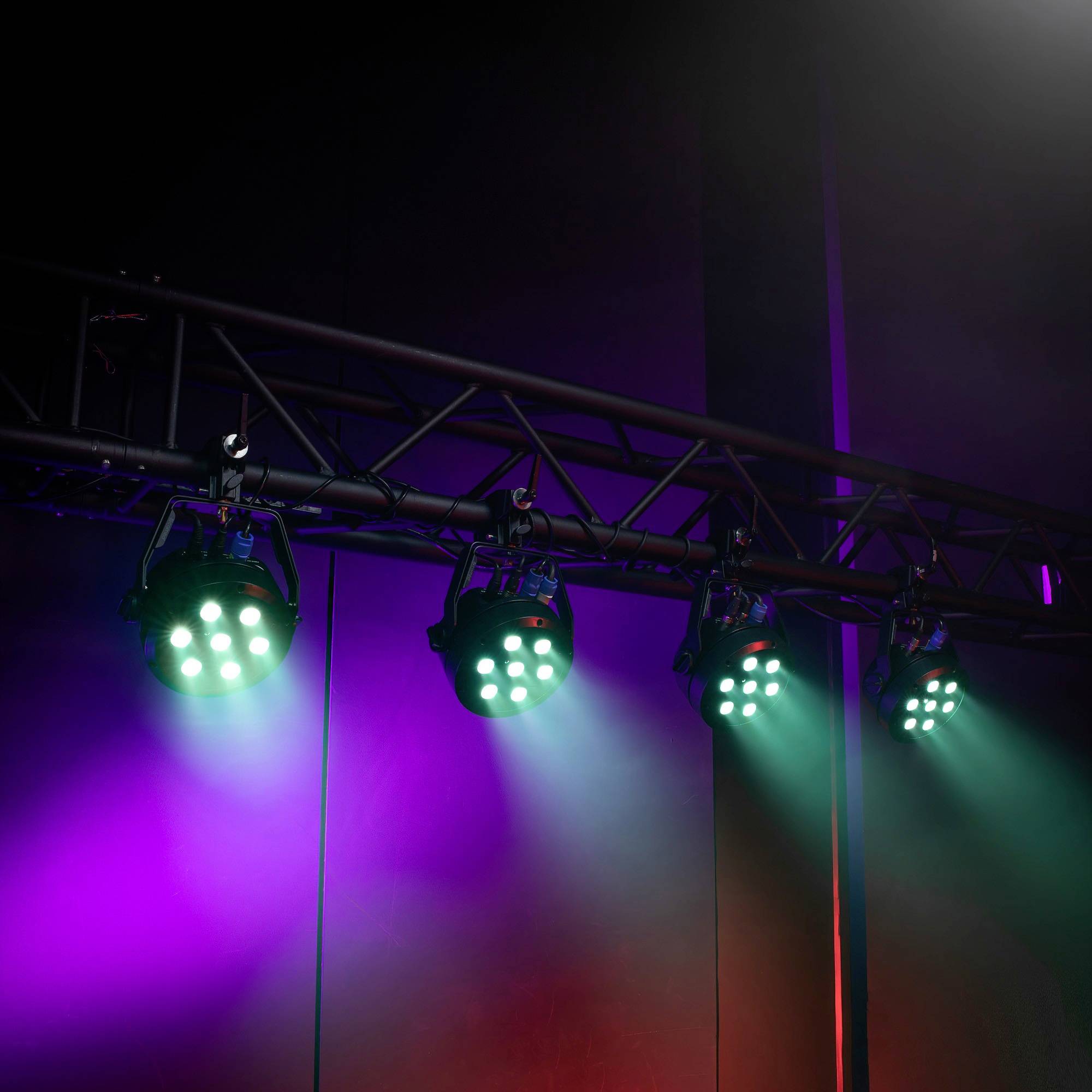 Bunte Bühnenlichter leuchten in Blau, Grün und Rot von einer metallenen Traverse, die eine stimmungsvolle Atmosphäre kreieren.