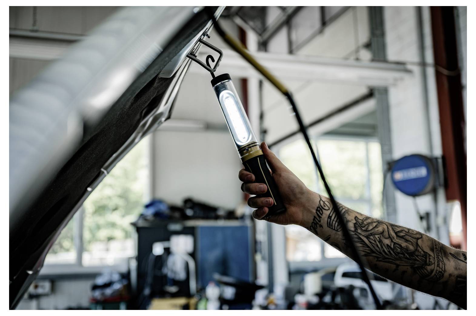 Mechaniker inspiziert einen Automotor mit einer tragbaren Arbeitsleuchte in einer Autowerkstatt.