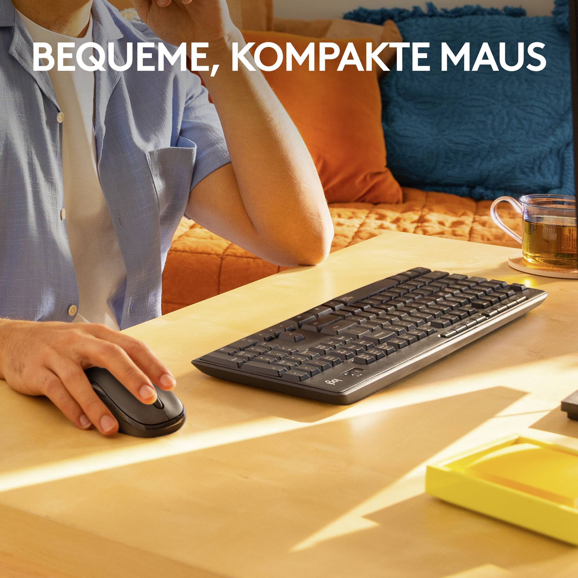 Eine Person am Schreibtisch hält eine ergonomische Maus in der Hand; daneben befinden sich Tastatur und Tasse. Text: 'Bequeme, kompakte Maus'.