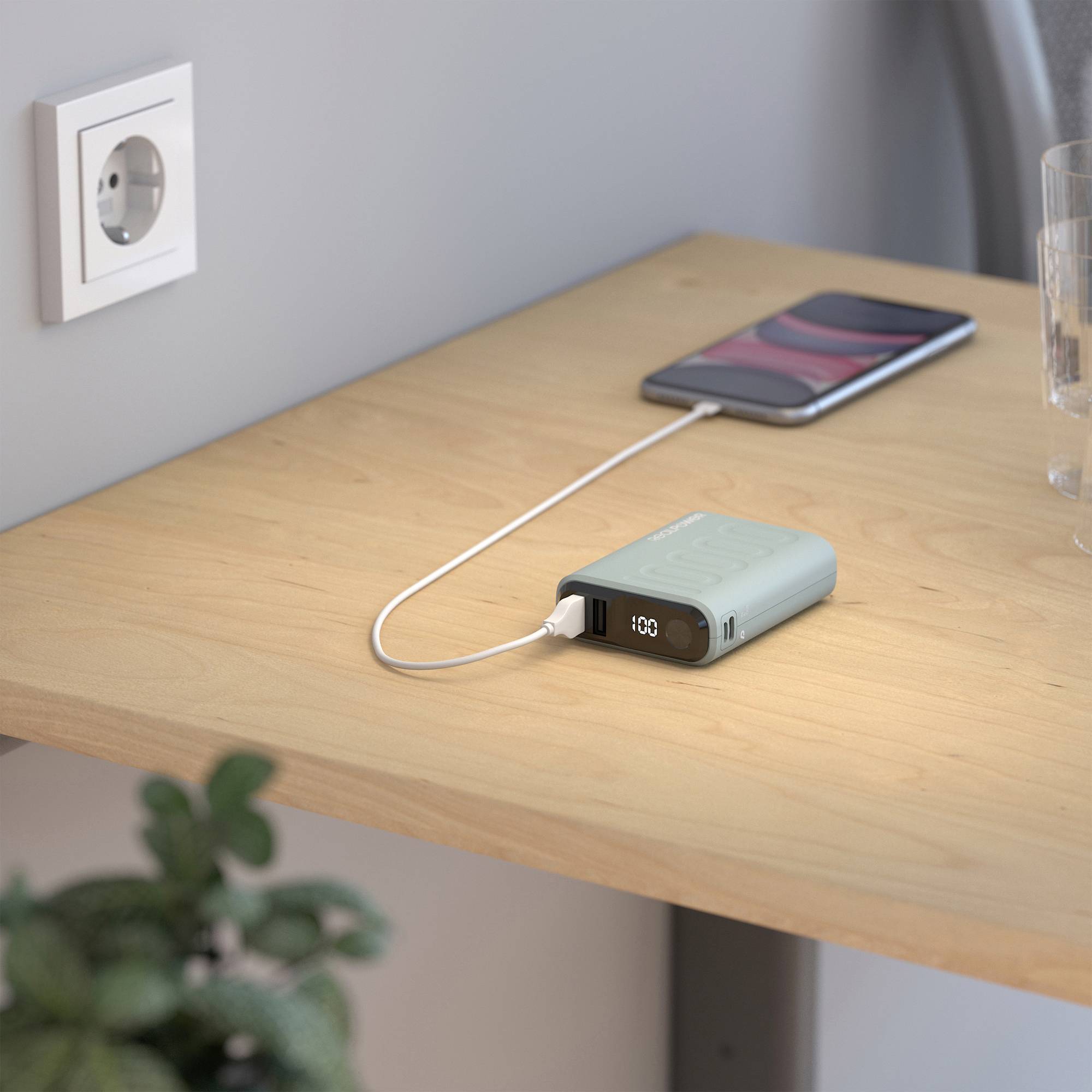 Ein Smartphone wird auf einem Holztisch über ein Kabel aufgeladen, das mit einer tragbaren Powerbank verbunden ist.