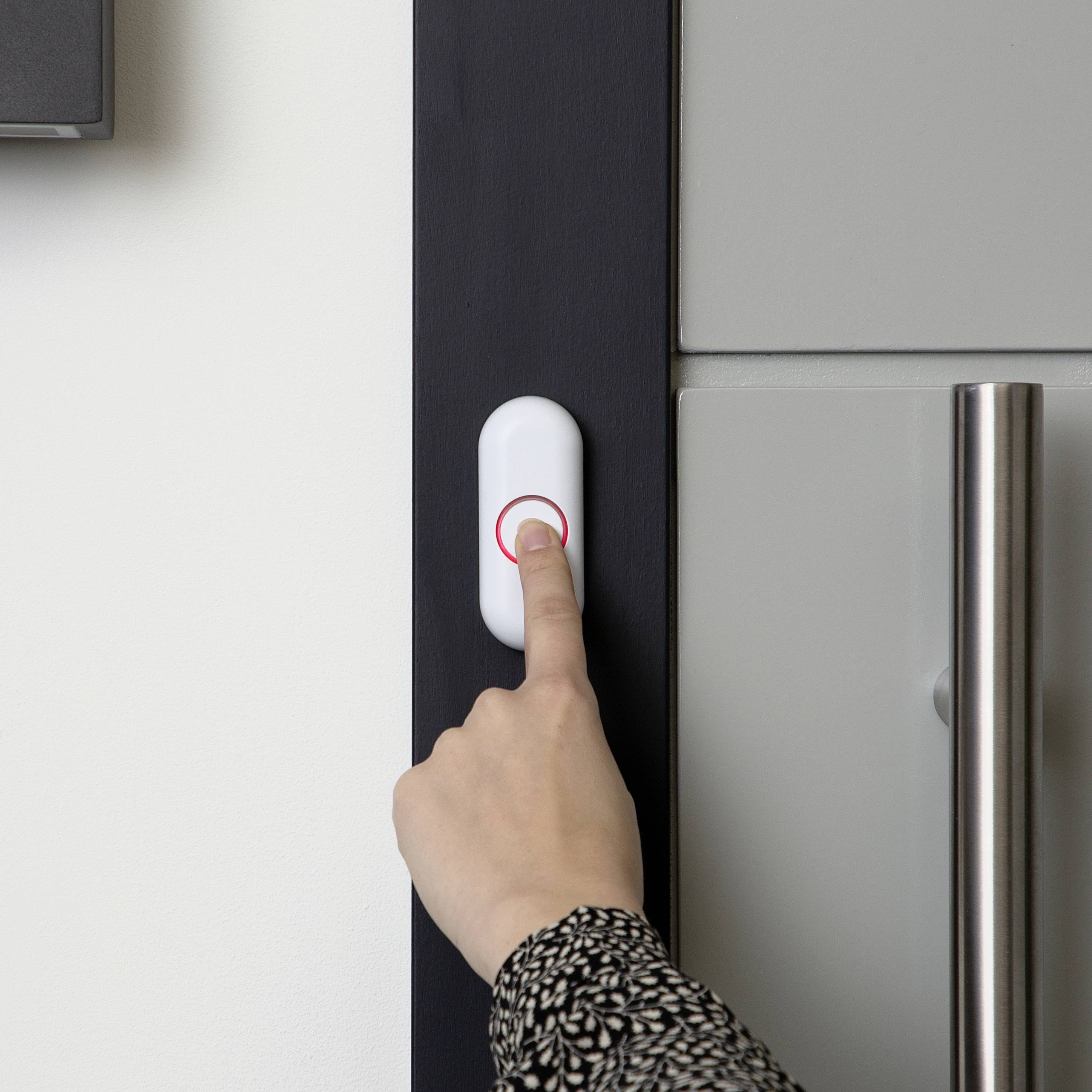 Eine Hand drückt eine Türklingel neben einer Tür mit silbergrauem Griff.