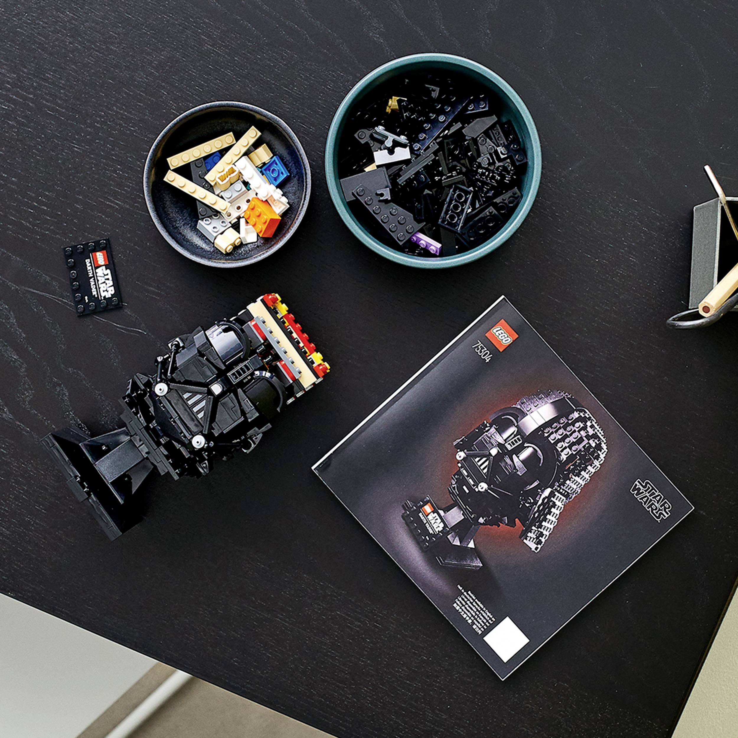 LEGO-Bausteine auf einem Tisch, darunter ein teilweise montierter Darth Vader-Helm und eine Anleitung.