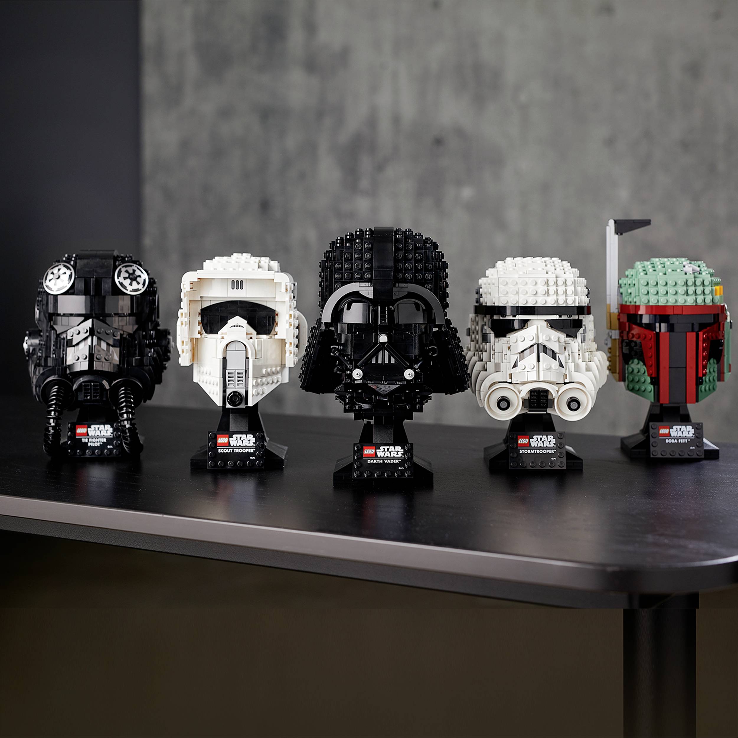 Fünf LEGO-Helm-Modelle von Star Wars-Charakteren, auf einem Tisch ausgestellt. Darunter Boba Fett, ein Stormtrooper und Darth Vader.