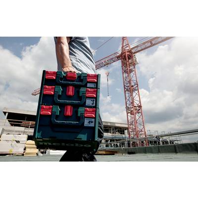 Person trägt eine Werkzeugkiste auf einer Baustelle. Im Hintergrund ein Kran und Gebäude im Bau. Himmel leicht bewölkt.