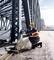 Ein Bauarbeiter mit Schutzhelm arbeitet an einer Eisenbrücke und verwendet ein Messgerät. Die Brücke erstreckt sich am Horizont.