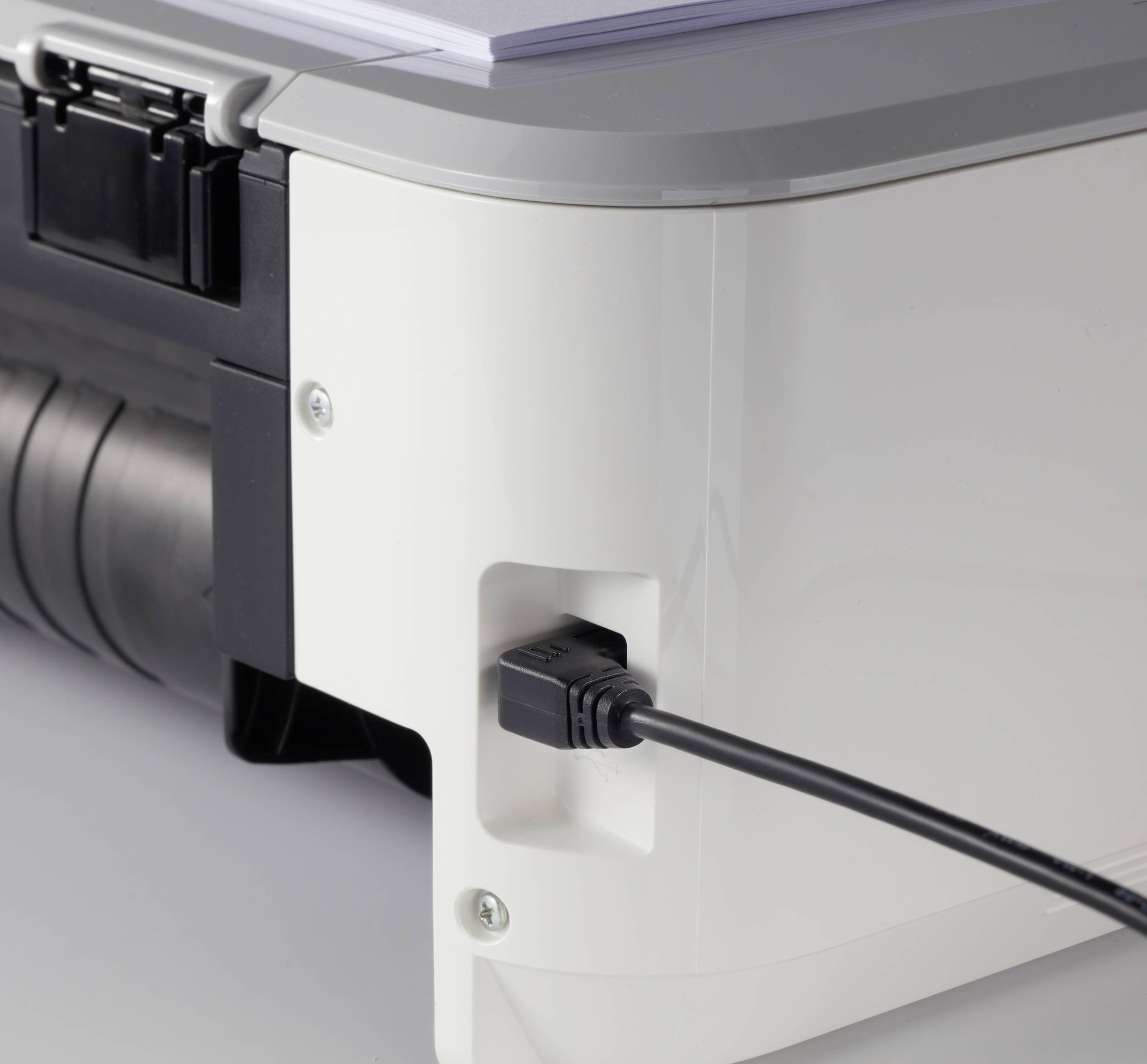 Ein Drucker mit einem USB-Kabel, das an der Seite angeschlossen ist. Oben liegt ein Stapel Papier bereit zum Drucken.