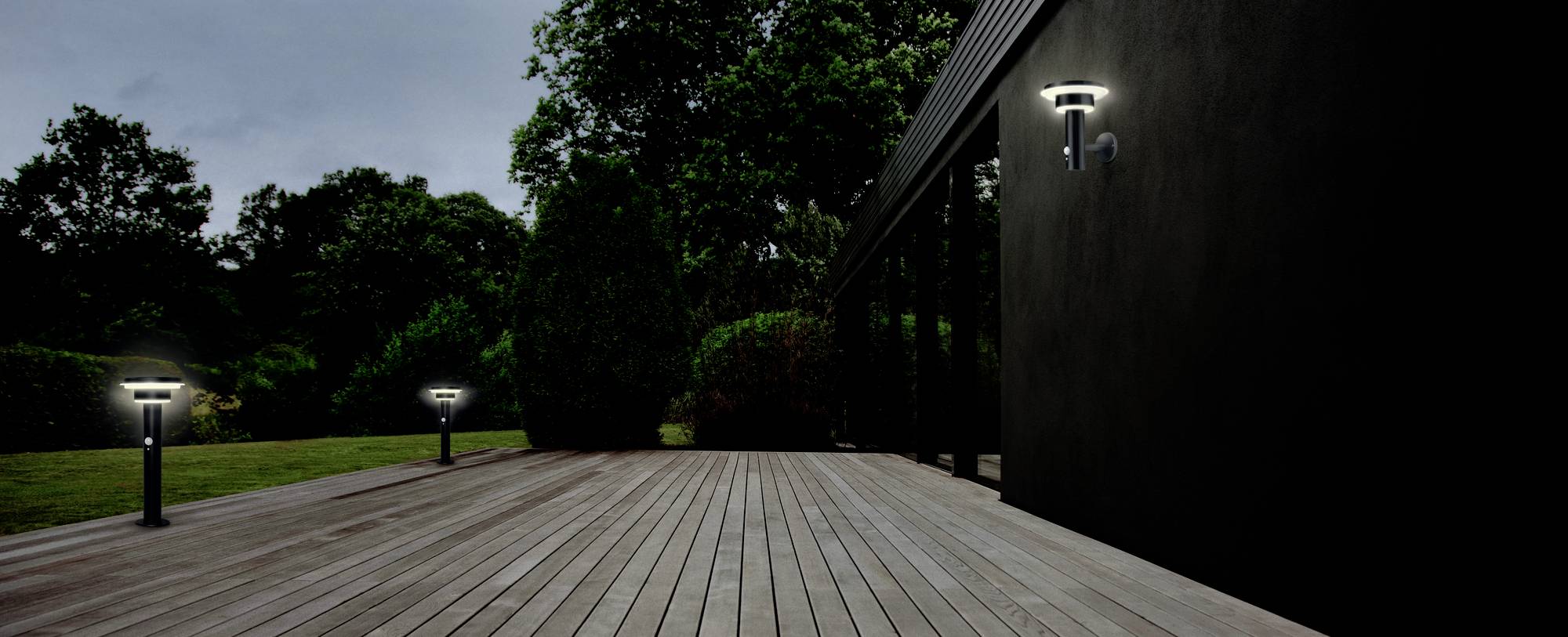 Eine Holzterrasse bei Nacht mit beleuchteten Lampen entlang des Weges und Bäumen im Hintergrund.