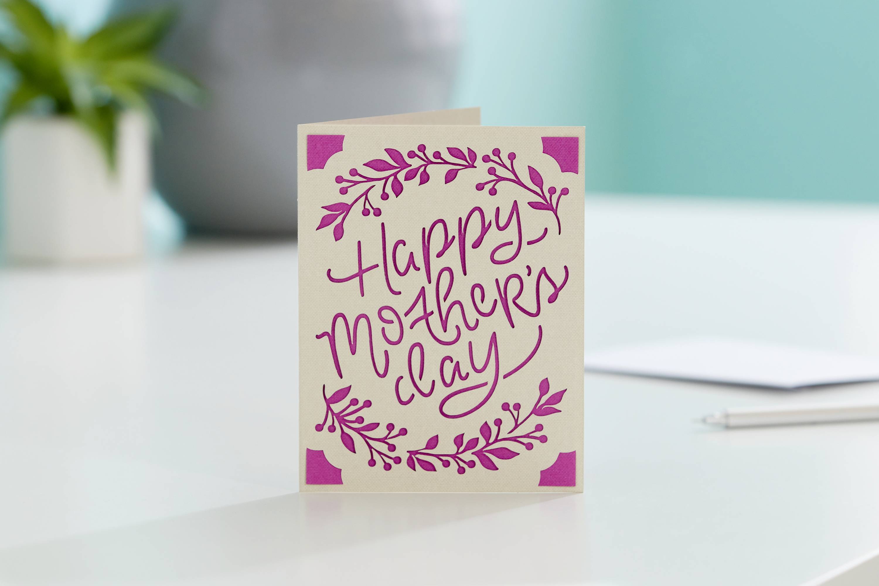 Grußkarte mit der Aufschrift 'Happy Mother's Day' und rosa floralen Verzierungen, steht auf einem Tisch.