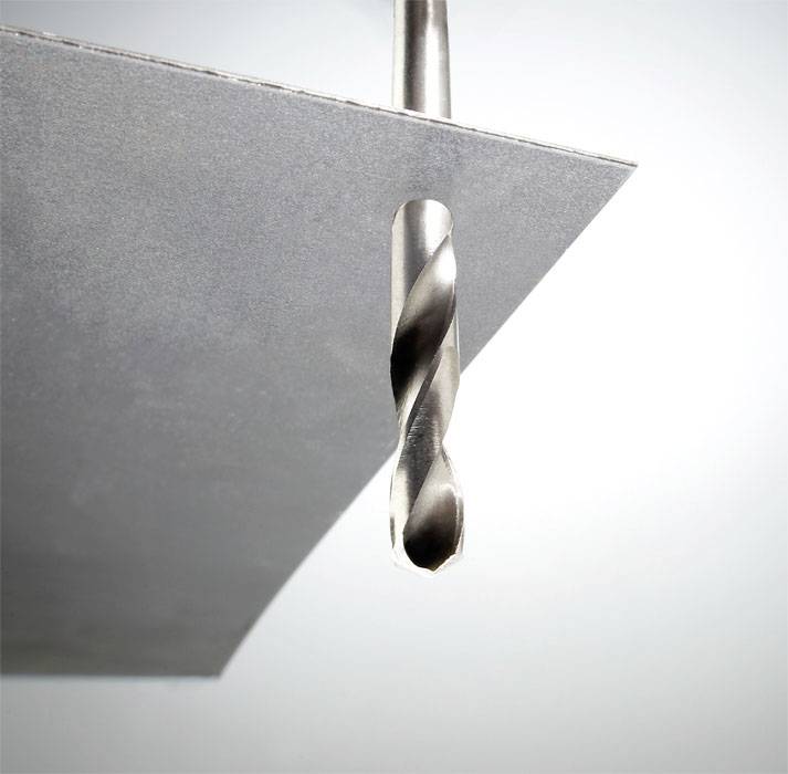 Ein Bohrer durchbohrt ein dünnes Metallblech, das von oben gehalten wird.
