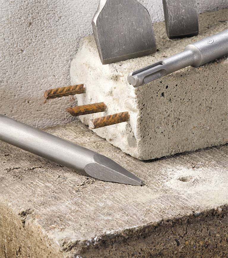 Werkzeuge auf Betonblock: Spitzmeißel, Flachmeißel, Hammerbohrer. Zeigt Anwendungsmöglichkeiten in der Bauindustrie.