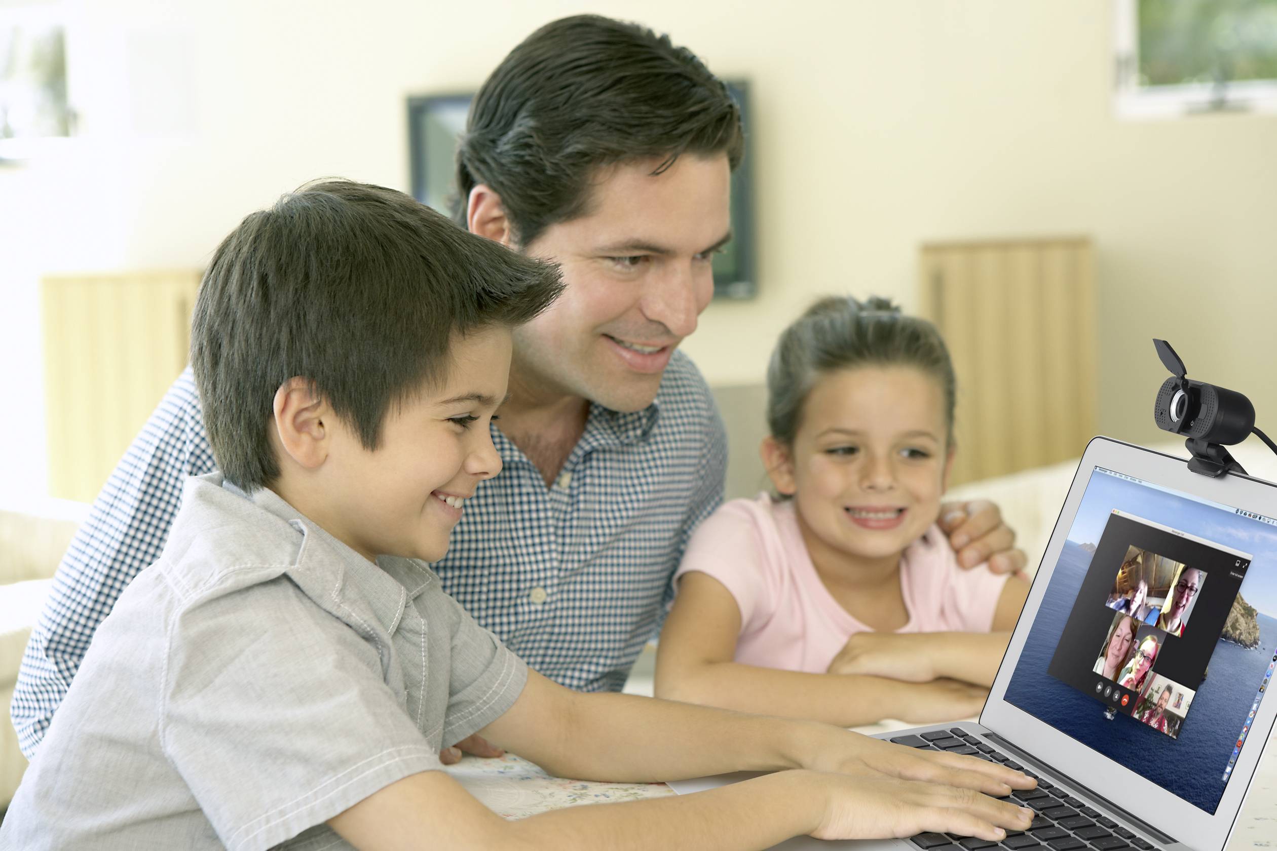 Ein Vater und zwei Kinder lächeln und schauen auf einen Laptop-Bildschirm. Sie führen einen Videoanruf mit mehreren Personen.