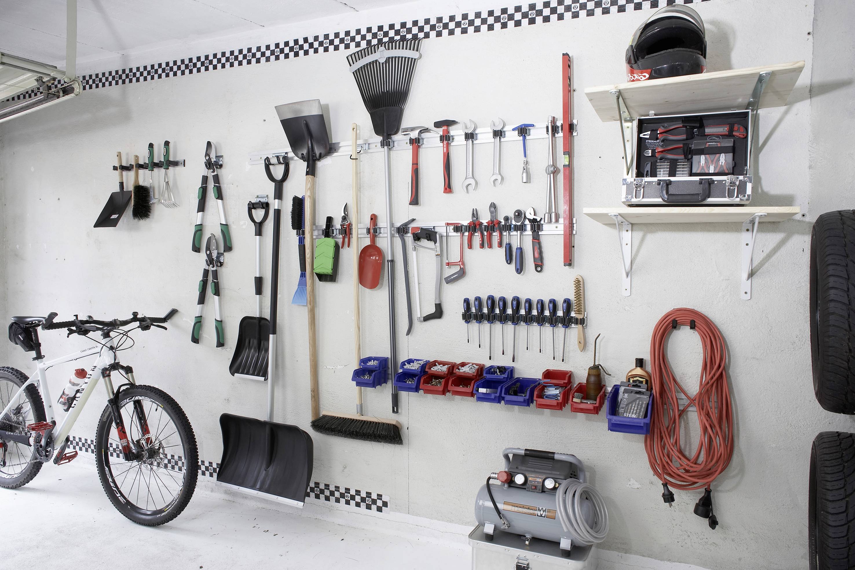 Eine Garage mit Werkzeugen an einer Wand, darunter Schaufeln, Besen, Schraubenschlüssel und ein Fahrrad, ordnungsgemäß angeordnet.