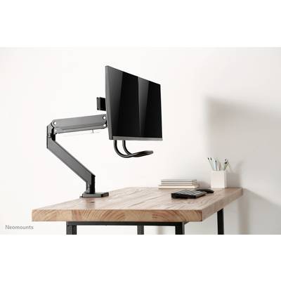 Ein Schreibtisch mit einem montierten Monitorarm, an dem ein Computerbildschirm hängt; daneben sind Stifte und Notizblöcke.
