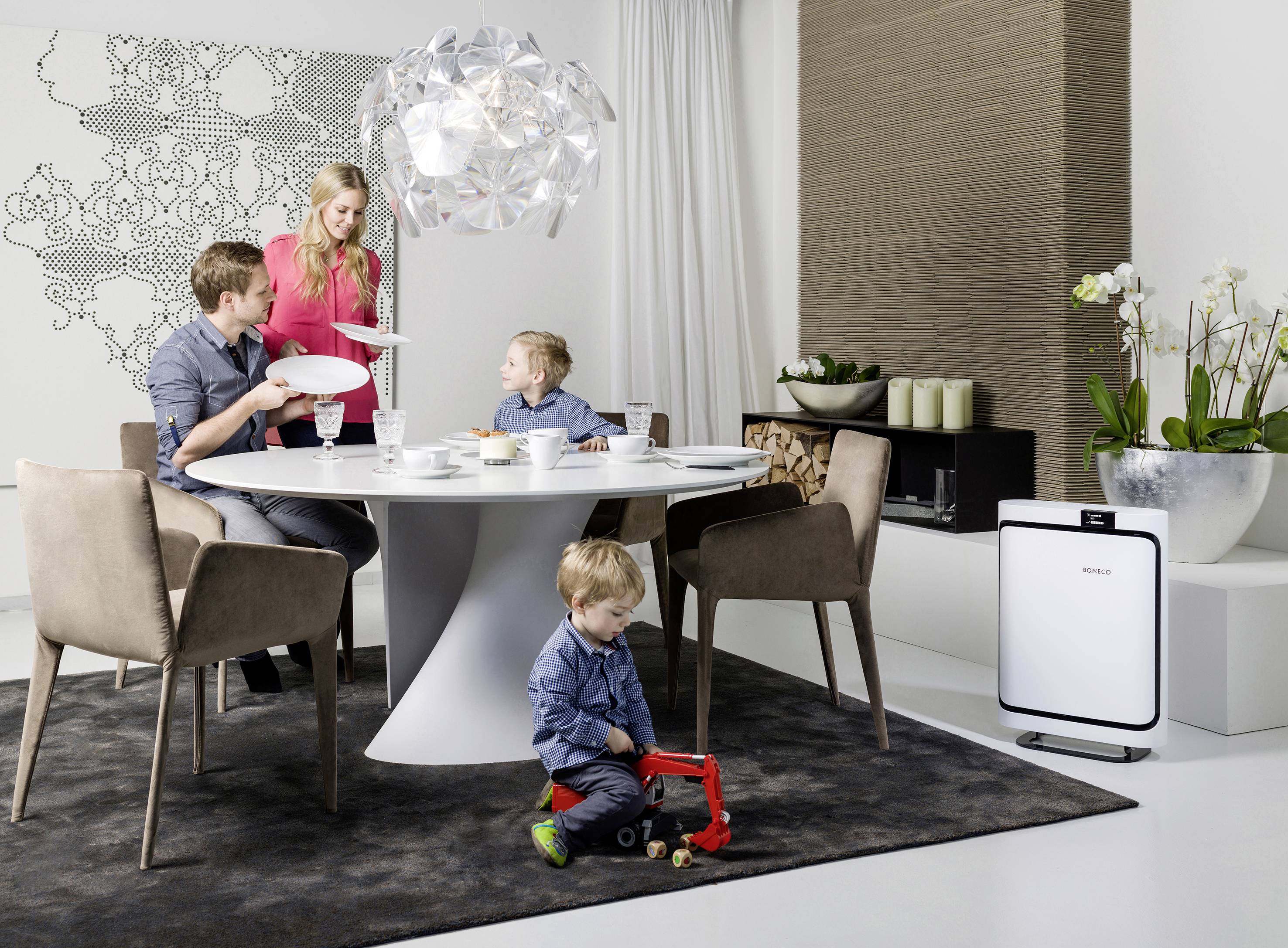 Eine Familie mit zwei Kindern frühstückt an einem modernen Esstisch. Ein Kind spielt mit einem Spielzeug-LKW auf dem Boden.