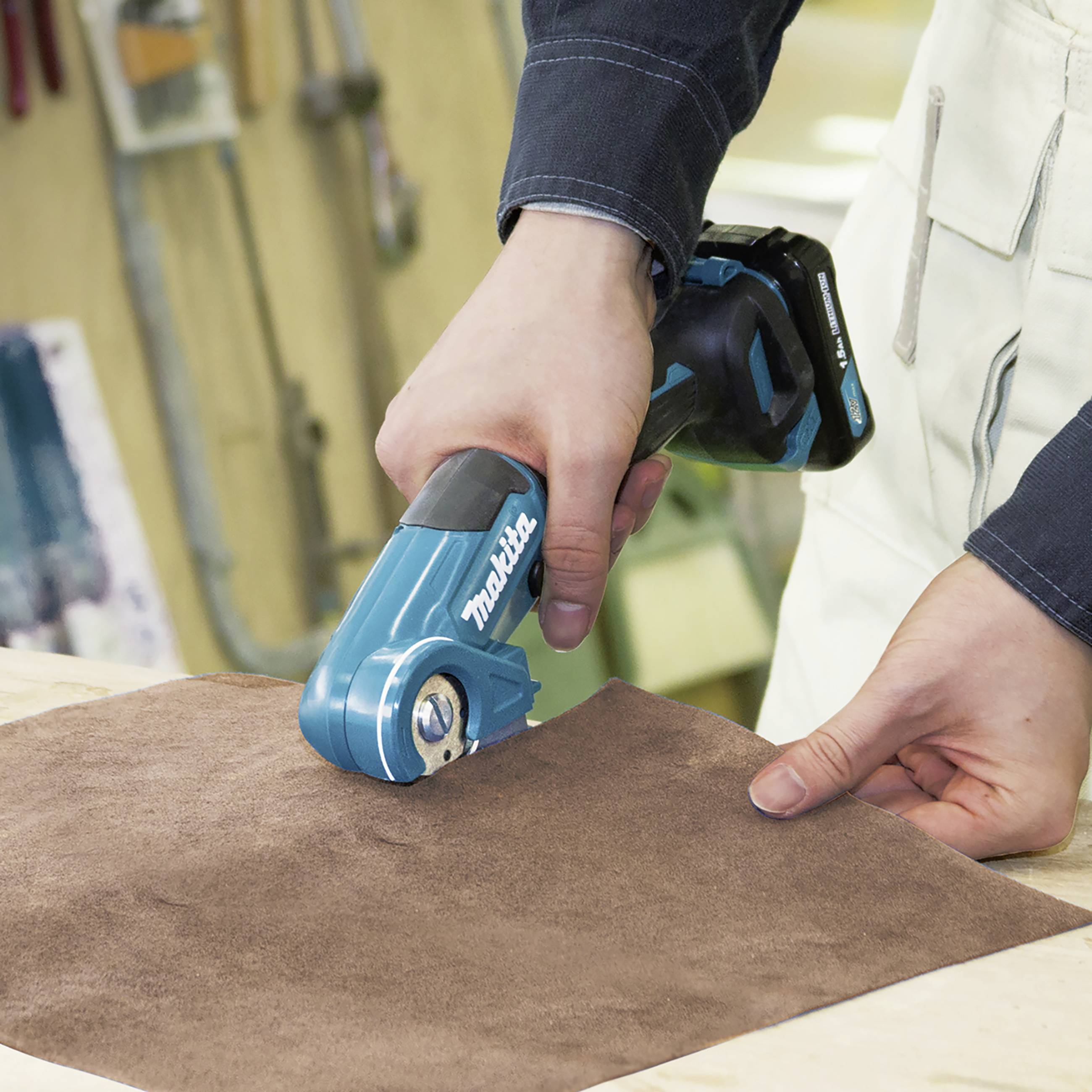 Eine Person schneidet mit einem blauen elektrischen Werkzeug auf einer braunen Oberfläche. Handschutz wird getragen.