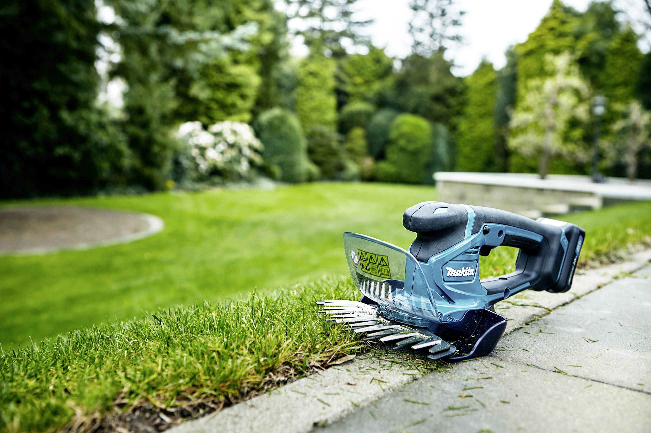 Ein elektrischer Rasenkantenschneider liegt auf einer gepflasterten Fläche neben sauber geschnittenem Gras in einem gepflegten Garten.