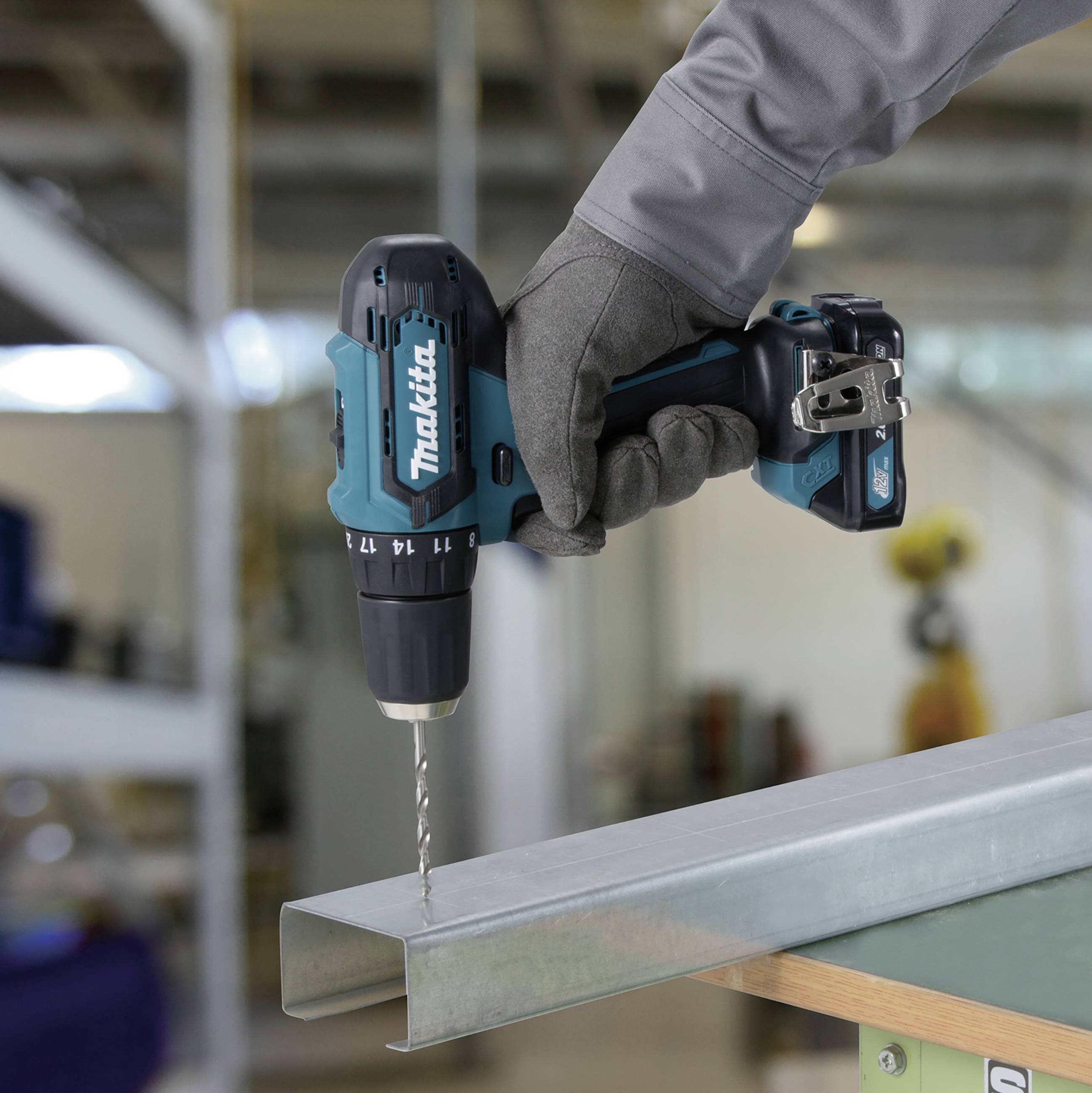 Eine Person bohrt mit einem Akkuschrauber ein Loch in einen Metallträger, während sie Grauhandschuhe trägt.