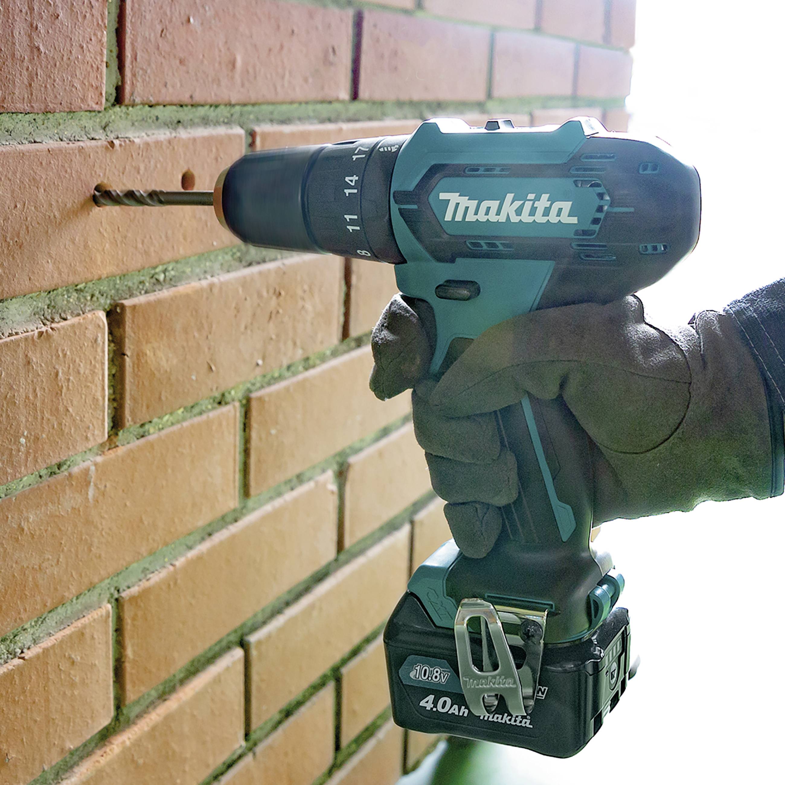 Eine Hand hält eine elektrische Bohrmaschine, die ein Loch in eine Ziegelwand bohrt. Die Maschine ist blau und von einer bekannten Marke.