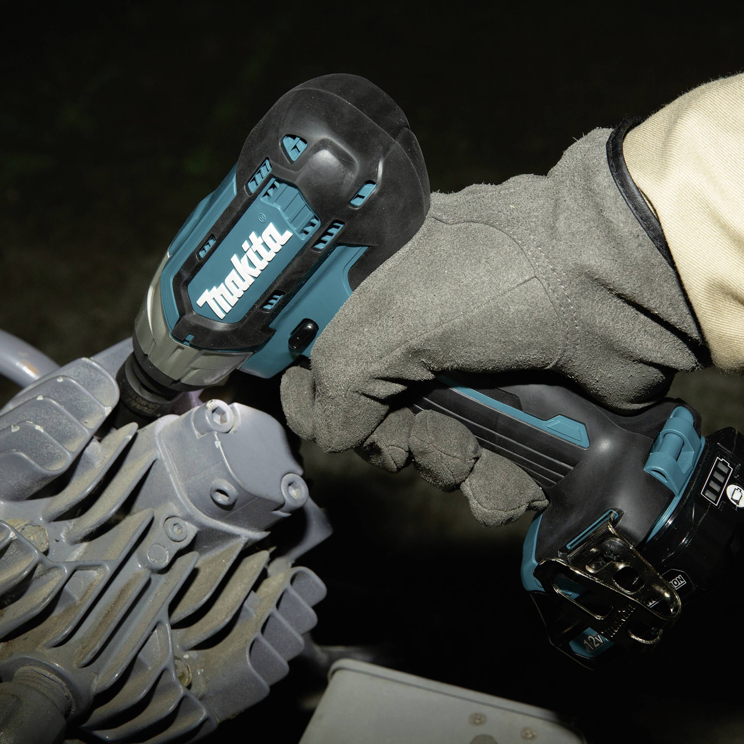 Eine Person trägt einen Handschuh und hält einen blauen Akkubohrer, der an einem mechanischen Gerät arbeitet.