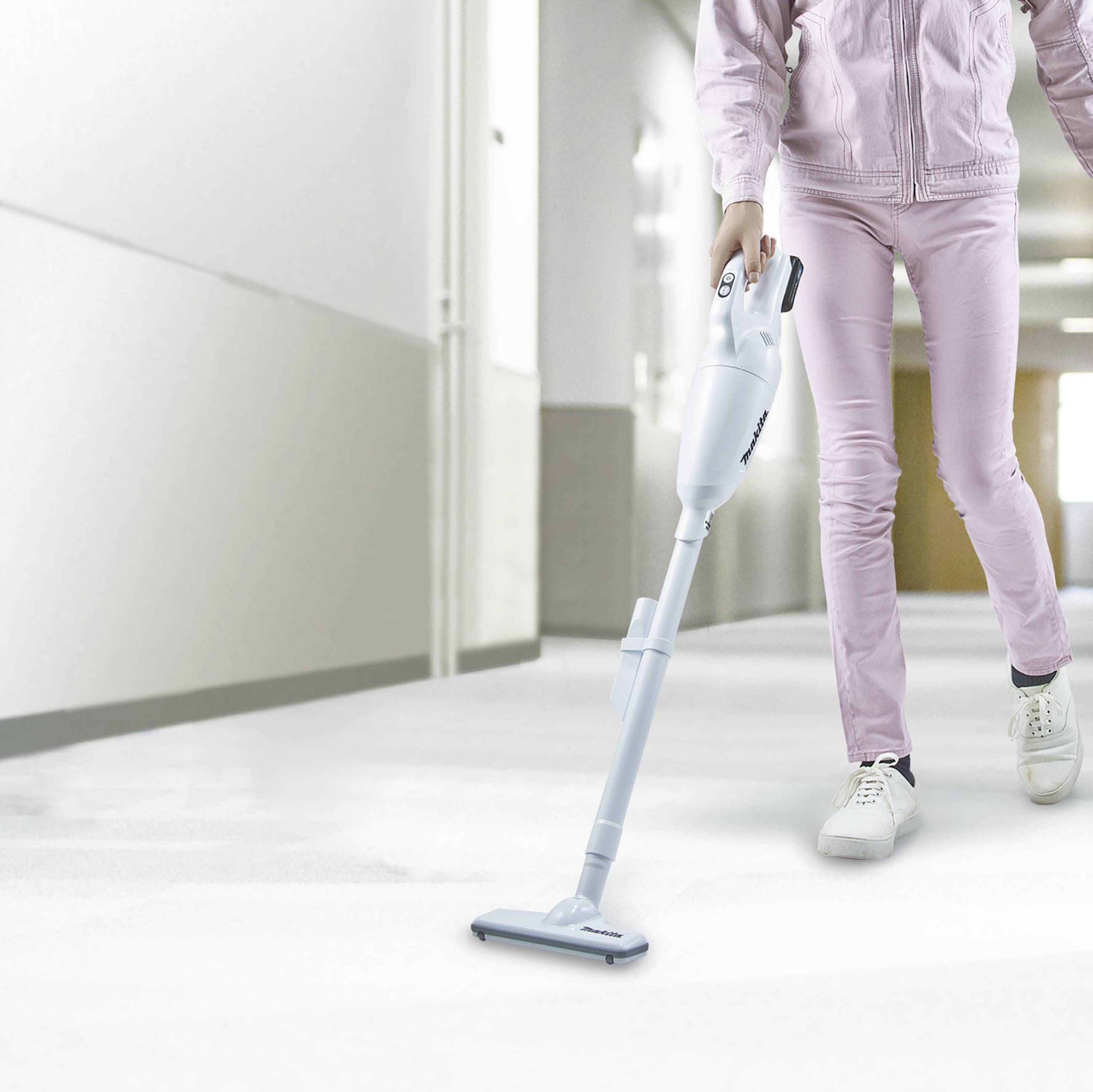 Person in einem rosa Trainingsanzug staubsaugt einen hellen Flur. Der Staubsauger ist kompakt und kabellos.