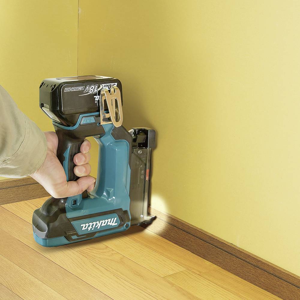 Eine Person verwendet einen kabellosen Nagler, um Holzfußleisten an einer Wand zu befestigen.