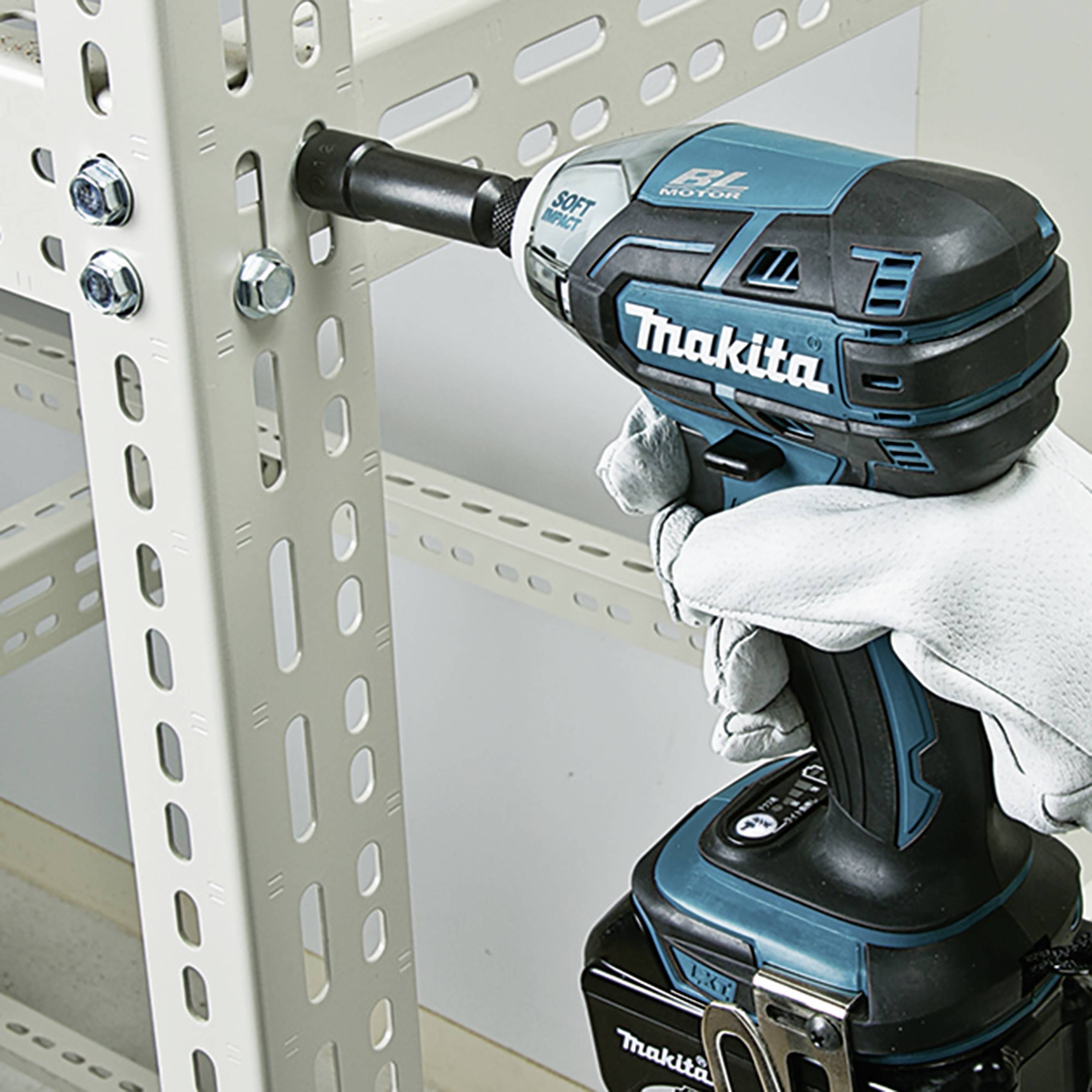 Eine Person mit weißen Handschuhen nutzt einen elektrischen Schraubenzieher, um eine Schraube in ein Metallregal zu drehen.