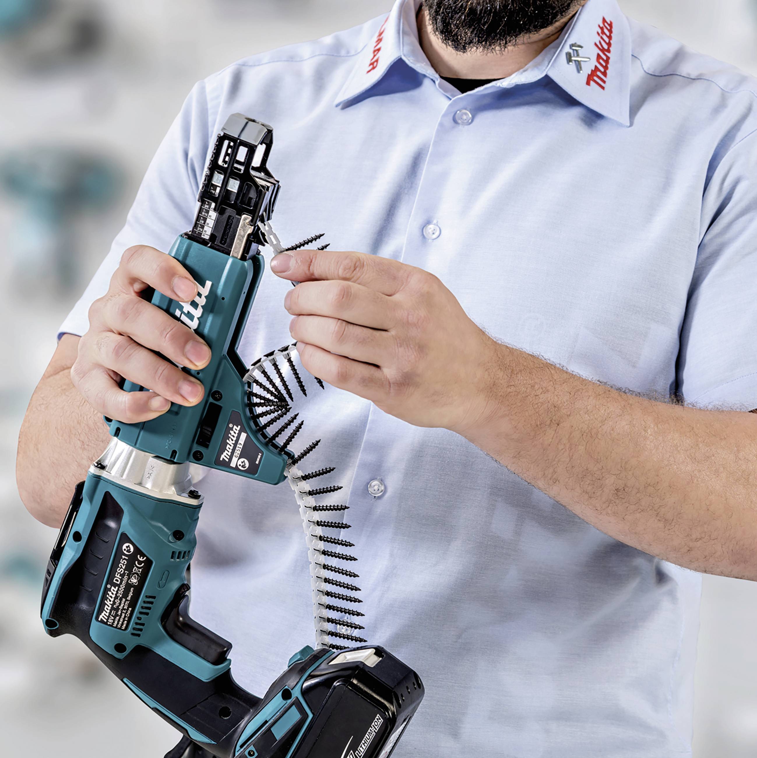 Eine Person hält einen elektrischen Schraubenzieher mit Magazin, bereit zur Verwendung. Sie trägt ein Hemd mit einem Markenlogo.