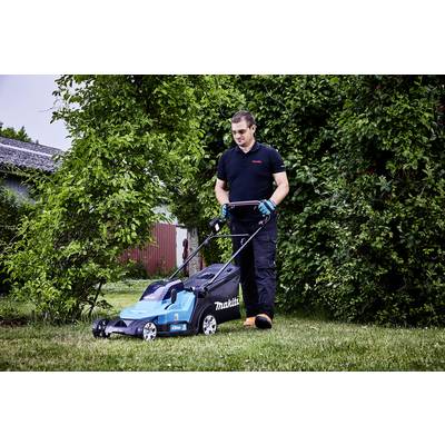 Ein Mann mäht einen Rasen in einem Garten mit einem blauen Rasenmäher. Im Hintergrund sind Büsche und ein Gebäude zu sehen.