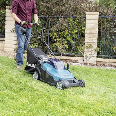 Eine Person mäht einen Rasen mit einem elektrischen Rasenmäher in einem Garten mit Rasenflächen und Zierpflanzen im Hintergrund.