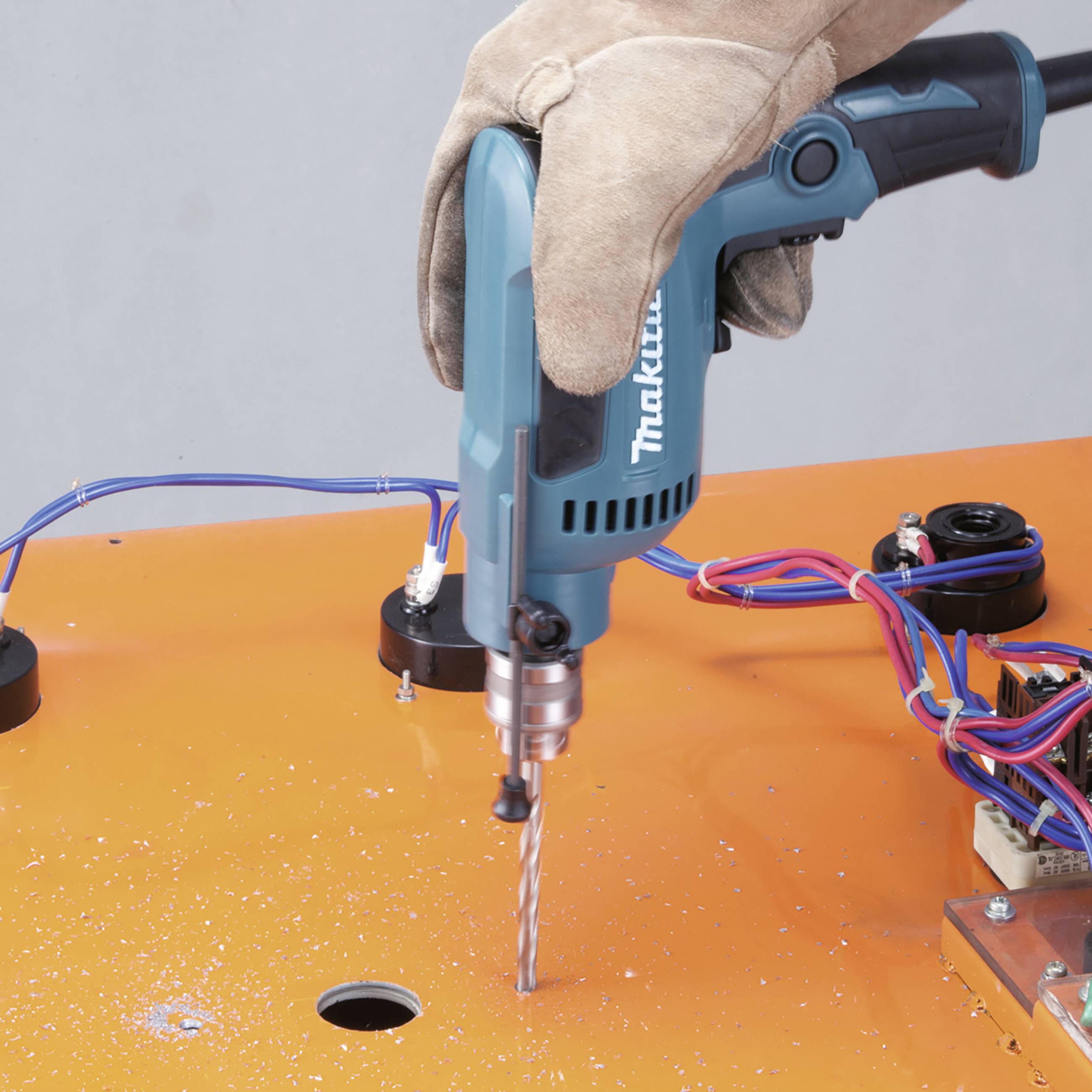 Eine Person bohrt ein Loch in orangefarbenes Material mit einer blauen Bohrmaschine. Elektrische Kabel sind zu sehen.