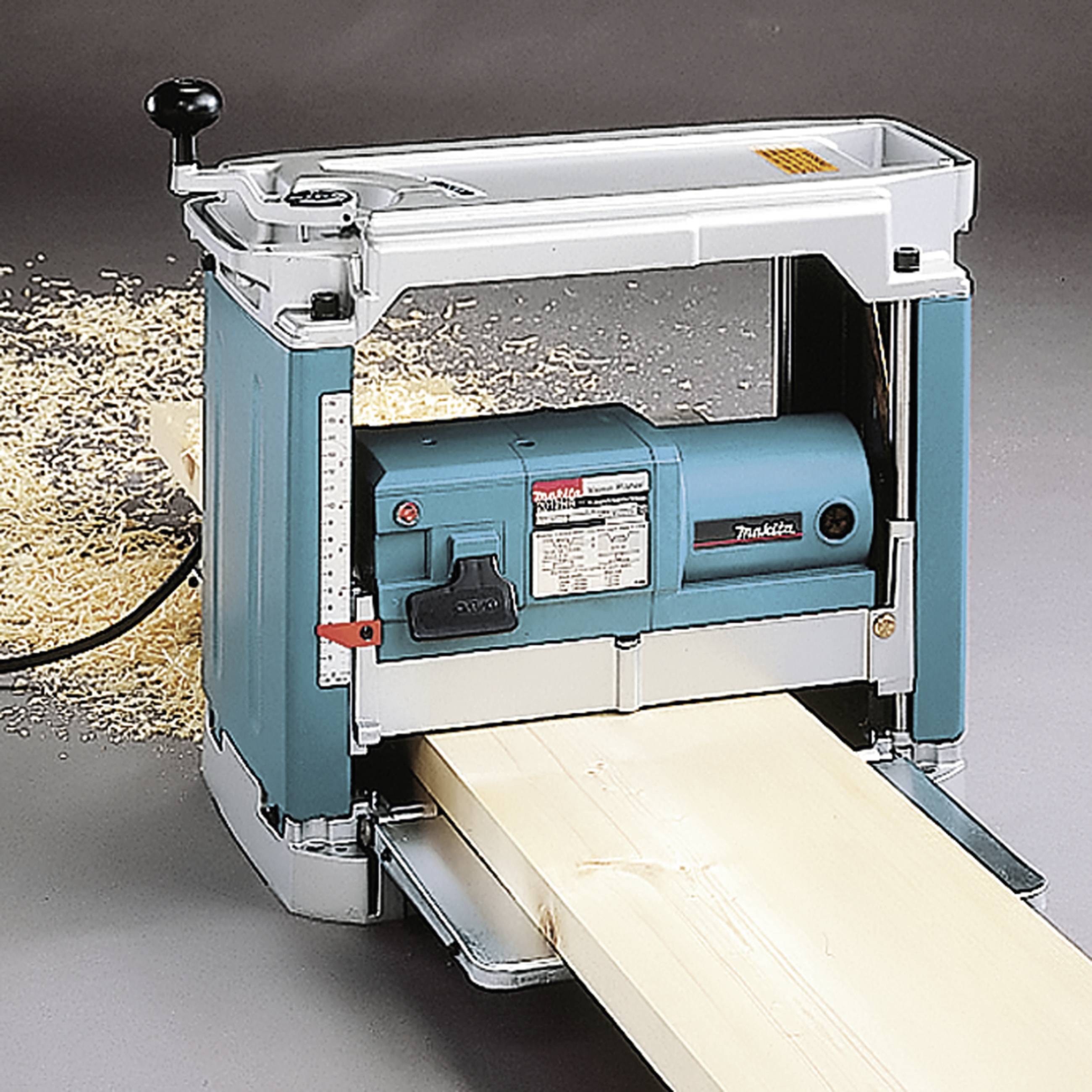 Holzbearbeitungsmaschine hobelt Holzbrette. Späne liegen auf dem Boden.