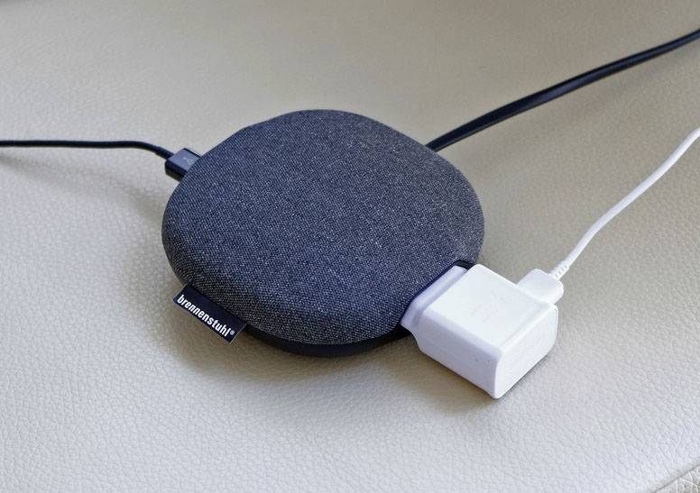 Flaches, rundes, schwarzes kabelloses Ladegerät mit angeschlossenem weißen USB-Kabel auf einer hellen Oberfläche.