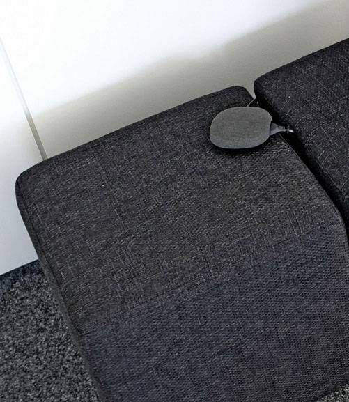 Ein graues Sofa mit einem kleinen, runden Kissen liegt auf einem Teppichboden in einem gut beleuchteten Raum.