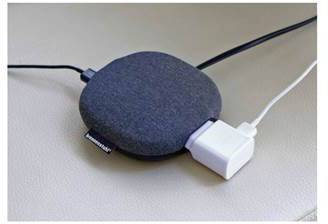 Ein rundes, graues Ladegerät mit Kabeln ist auf einer Oberfläche platziert. Es lädt ein elektronisches Gerät.