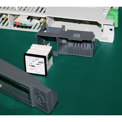 Elektrisches Messgerät (Amperemeter) und andere Bauteile auf einem grünen Tisch, in einer Werkstatt oder technischen Umgebung.