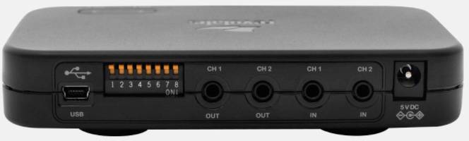 Schwarzes elektronisches Gerät mit Schaltern und Anschlüssen, darunter USB-Port links. Vier Audioanschlüsse zur Steuerung von Ausgängen und Eingängen.