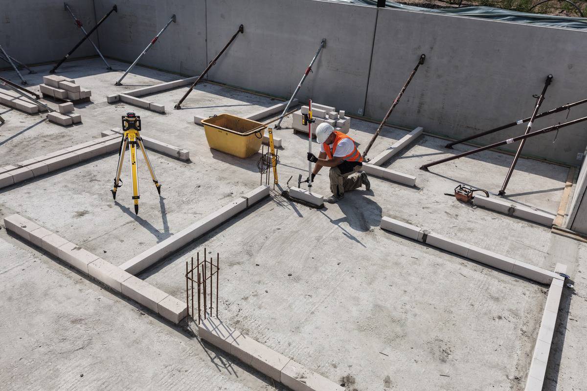 Ein Bauarbeiter in Schutzkleidung arbeitet an Grundrissen mit Mauersteinen und Bauwerkzeugen auf einer Baustelle.