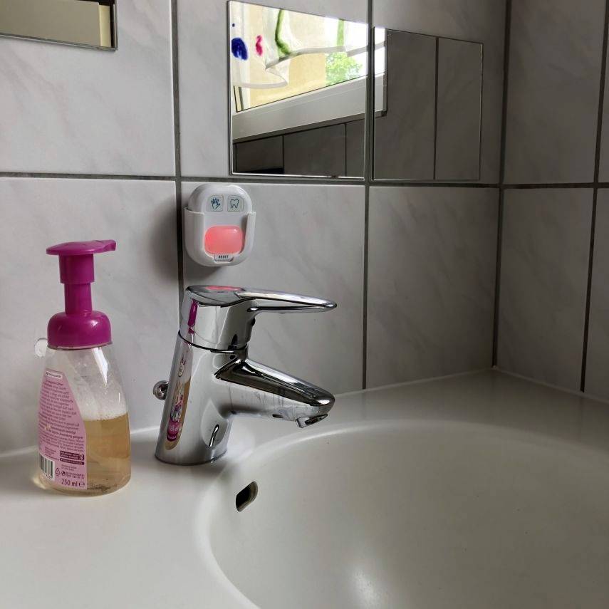 Ein Badezimmerwaschbecken mit Chrom-Wasserhahn und rosa Flüssigseifenspender. Oben ist ein kleines Fenster zu sehen.