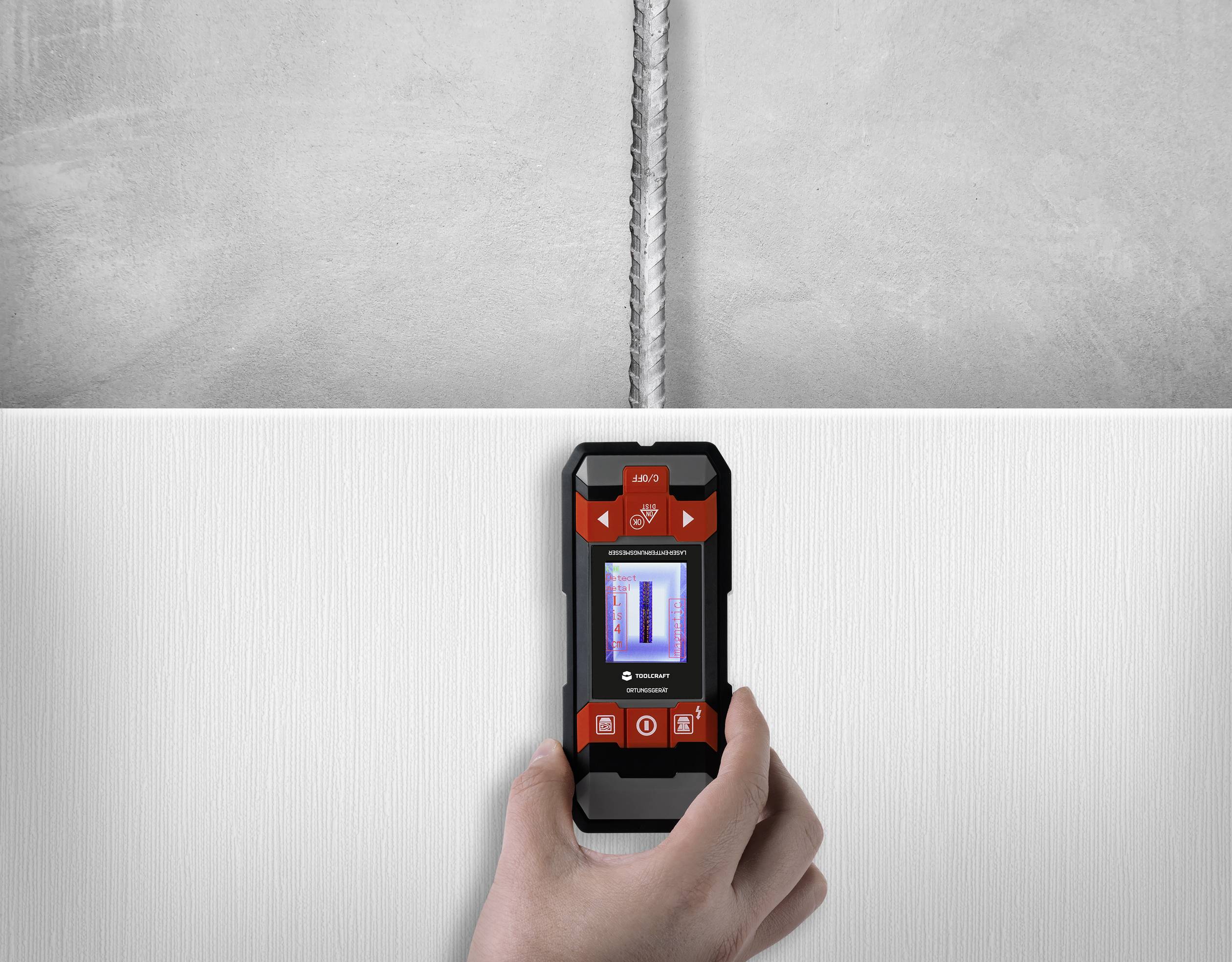 Eine Hand hält ein Wandscannergerät, das ein Rohr hinter der Wand lokalisiert. Das Gerät zeigt die Position auf einem kleinen Bildschirm an.