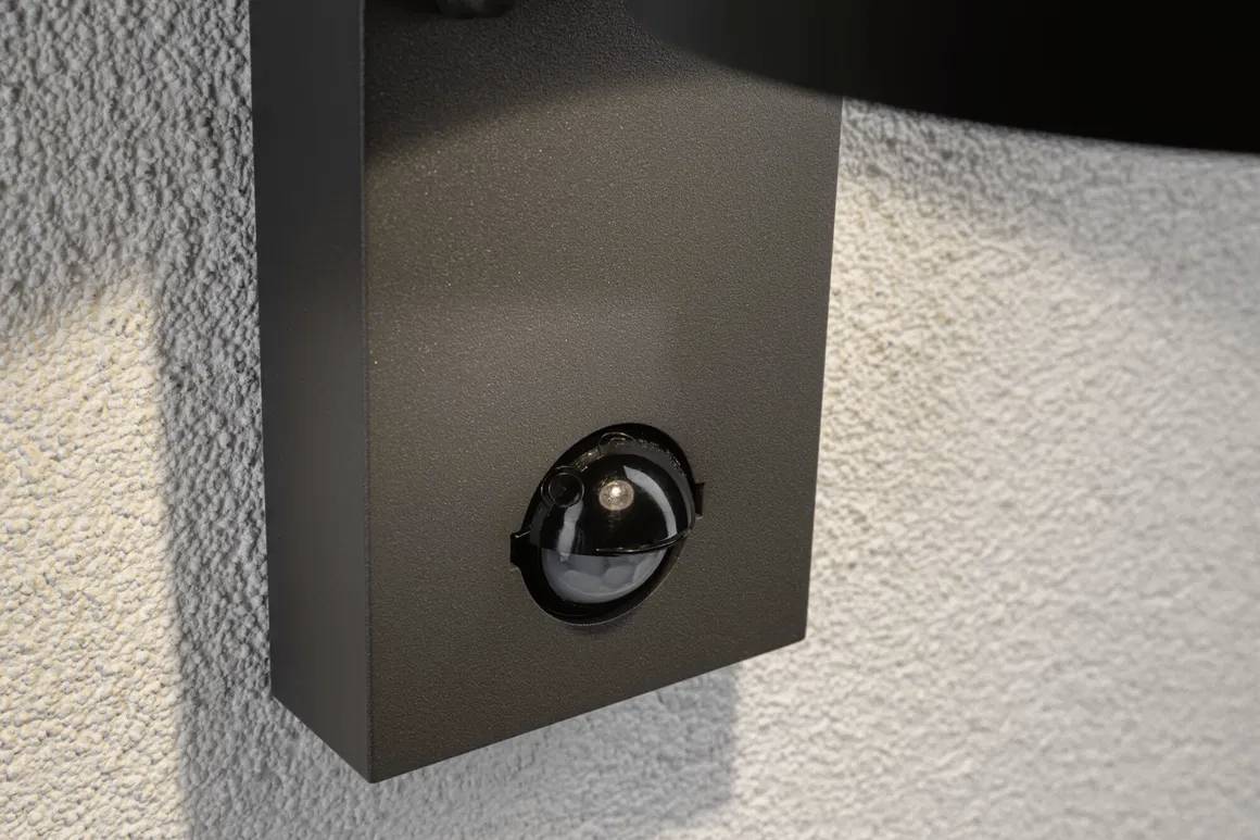 Schwarze Überwachungskamera an einer Wand montiert, leicht abgewinkelt, um den Bereich darunter zu erfassen.