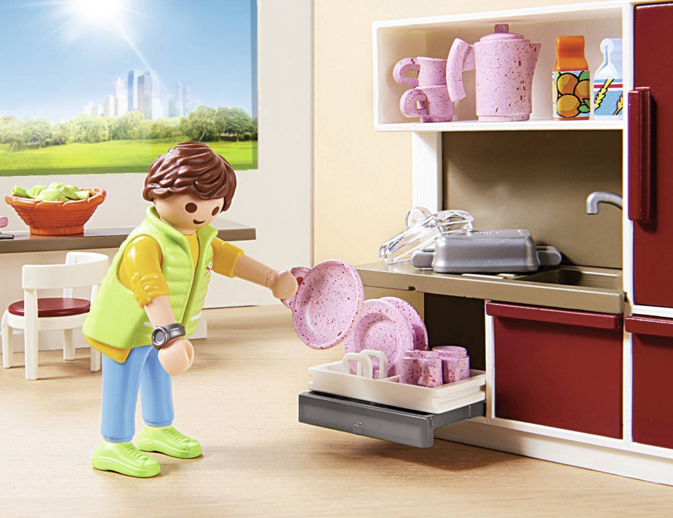 Playmobil-Figur stellt rosa Geschirr in den Geschirrspüler einer Puppenküche. Im Hintergrund sind ein Fenster mit Stadtlandschaft und ein Tisch mit Obst zu sehen.