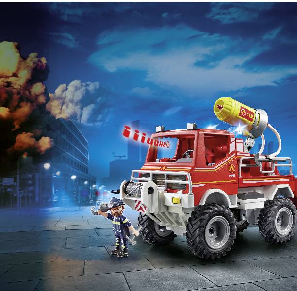 Ein rotes Spielzeug-Feuerwehrauto mit einem gelben Wasserschlauchaufsatz steht auf einer Straße, daneben eine Spielfigur eines Feuerwehrmanns. Im Hintergrund brennt ein Gebäude.